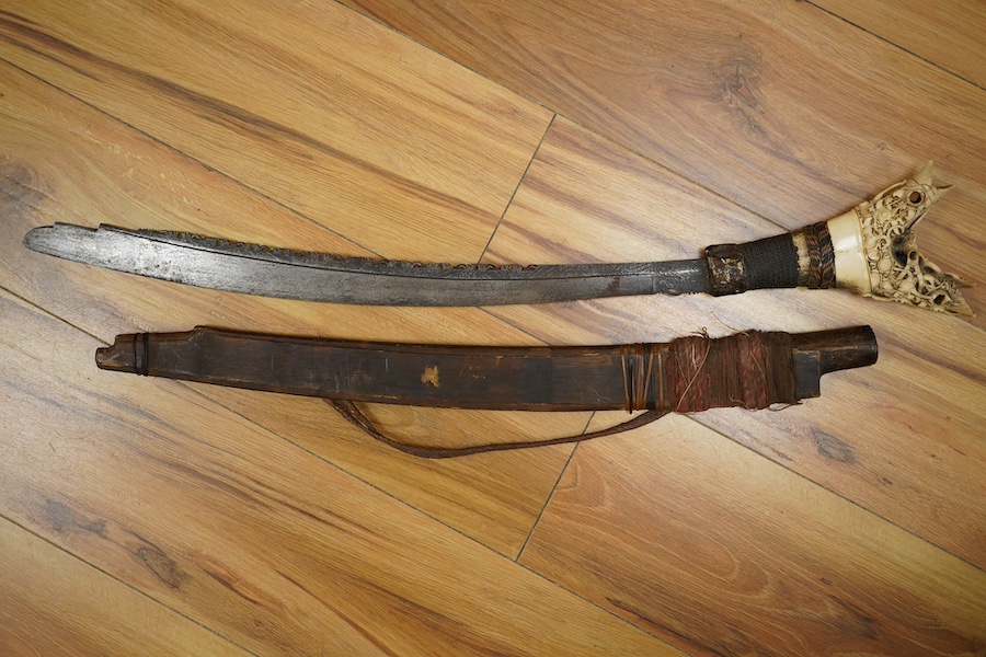 An elaborate Dayak headhunter’s sword Mandau, curved blade with chiselled and engraved back edge, large bone grip carved with protruding teeth, etc. in its wooden scabbard. Condition - good, some age wear.